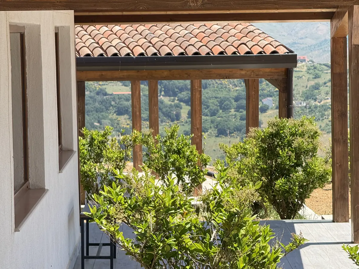 Il portico con la tettoia in legno e gli alberelli, aperto sulla valle