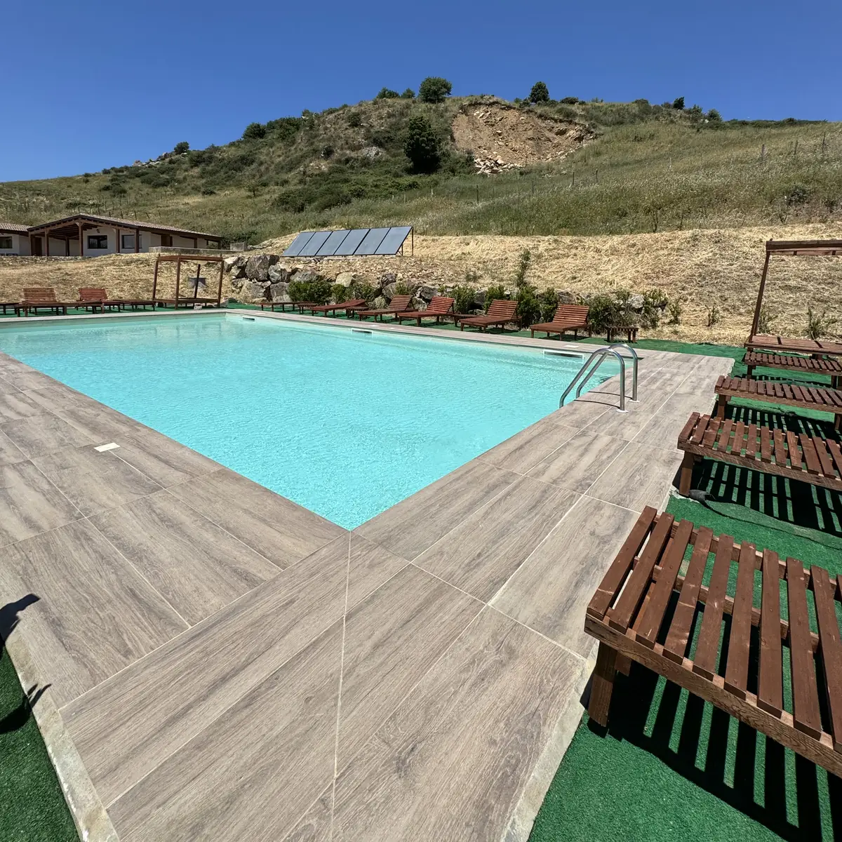La piscina con il bordo in legno e i lettini, le colline dei Nebrodi dietro