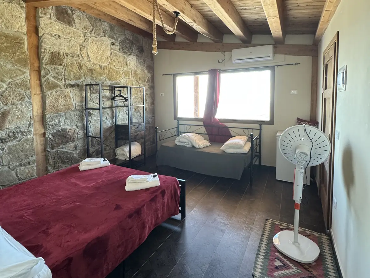 Camera Classica: la parete di pietra viva, le travi a vista e il letto in velluto rosso