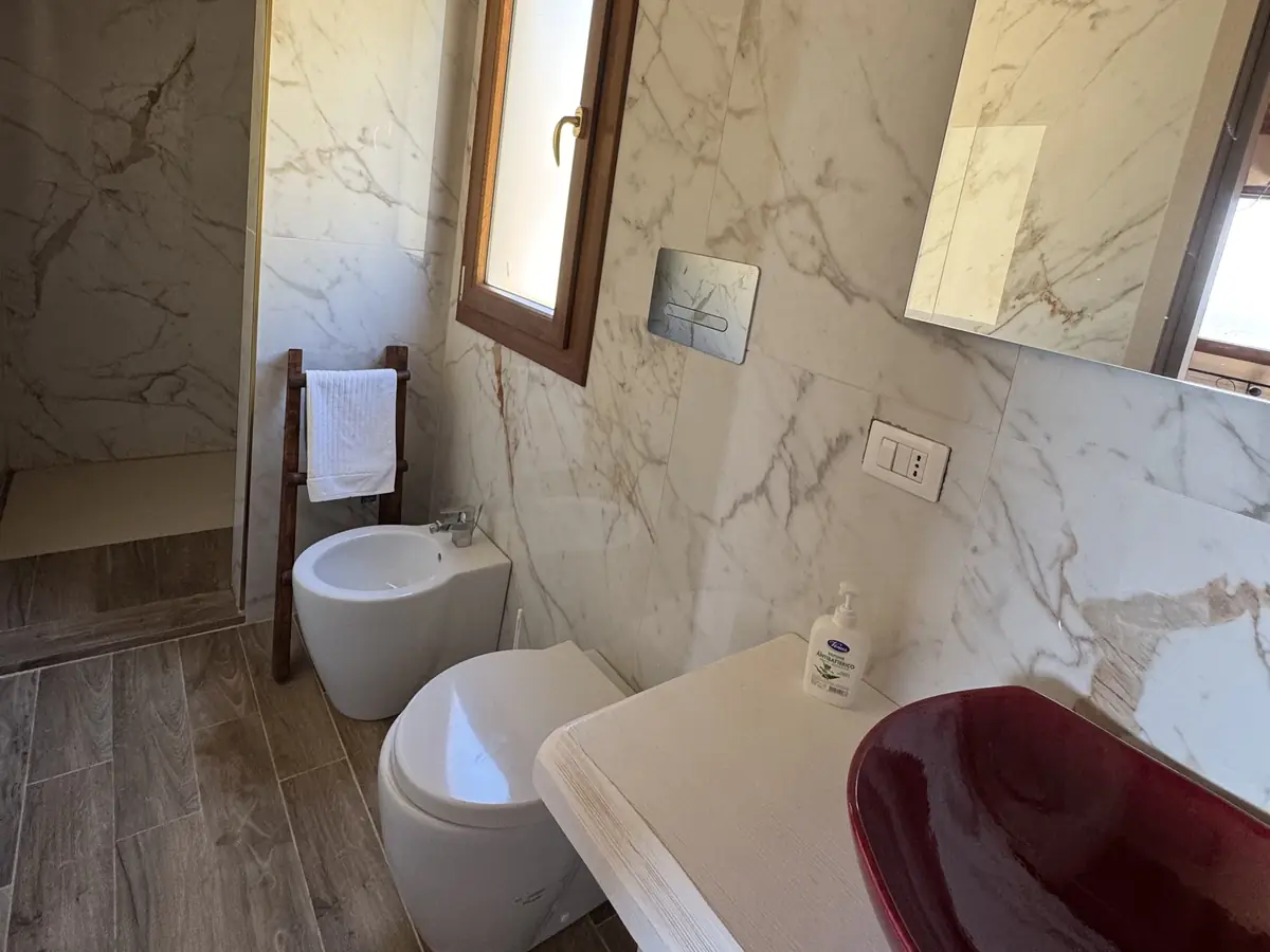 Il bagno con il lavabo rosso sul piano e la parete effetto marmo