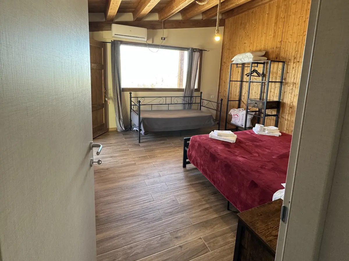 La camera vista dalla porta: travi, parete in legno e letto rosso