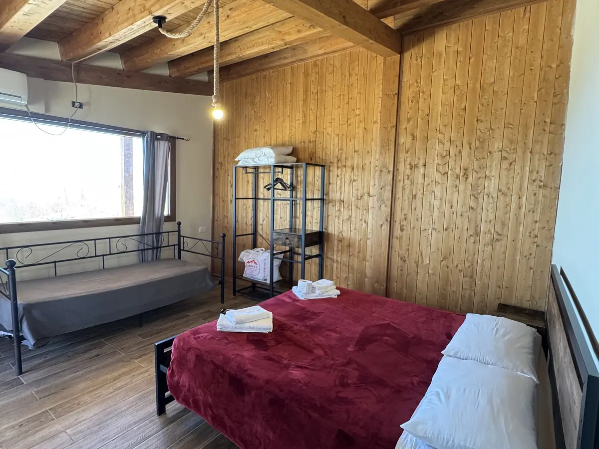 La camera con le pareti in legno, il soffitto a travi e il letto rosso