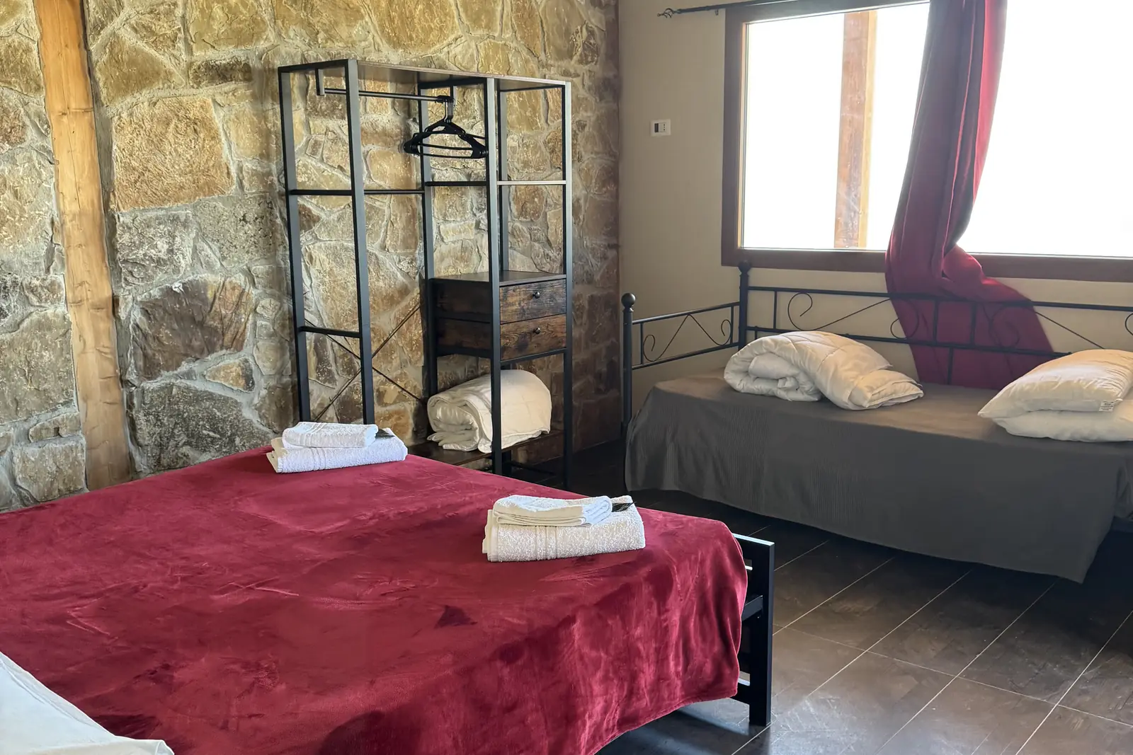 Una delle camere: la parete di pietra viva, la finestra sulla campagna e il letto in velluto rosso