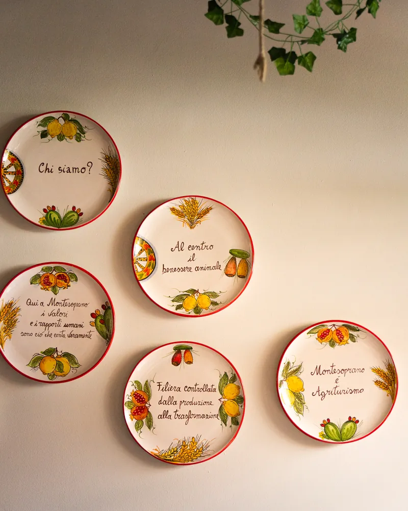 Cinque piatti di ceramica dipinti alla parete della ristomacelleria di Milano; il primo dice «Chi siamo?»
