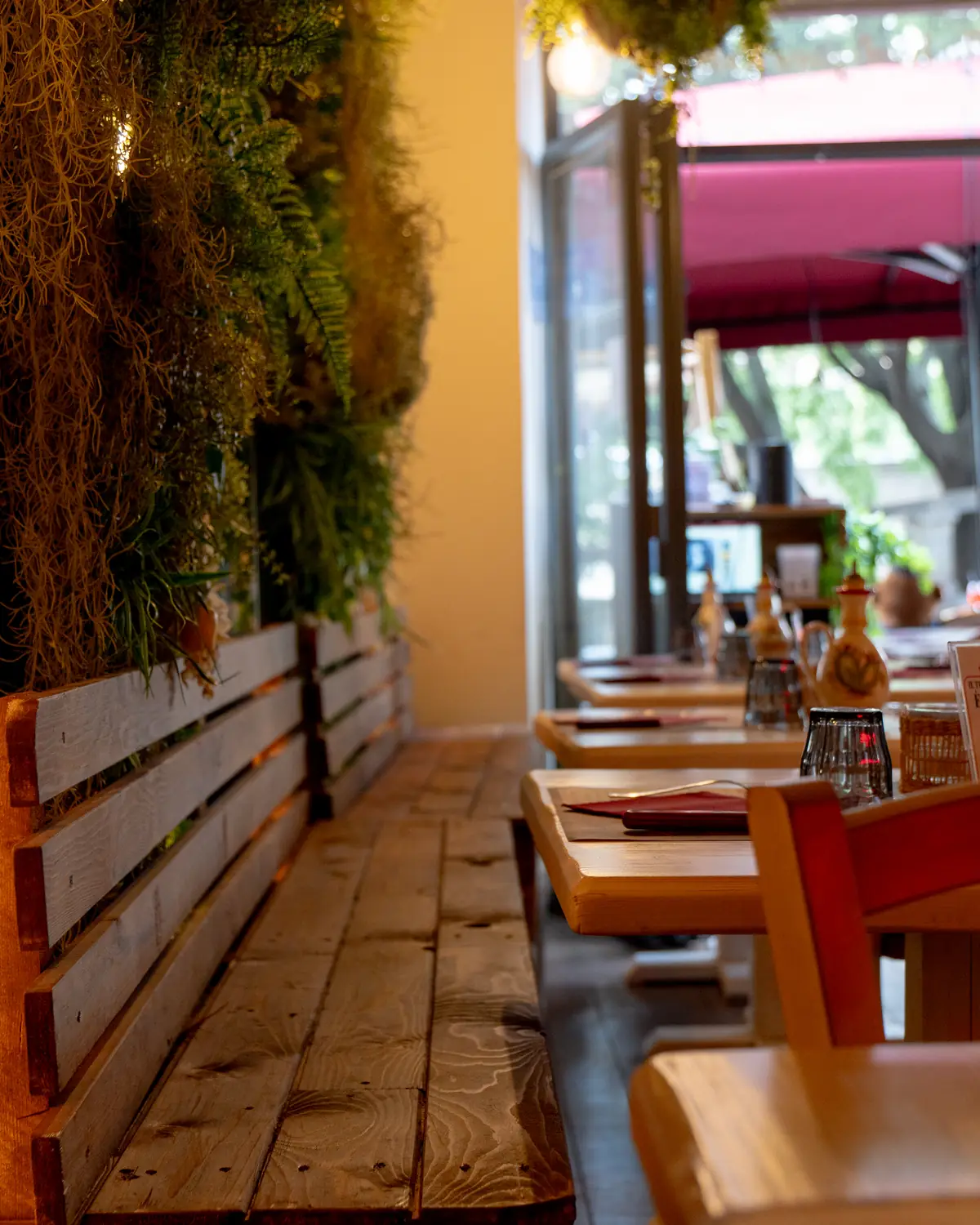 La sala di una ristomacelleria di Milano: panca di legno, tavoli apparecchiati e la vetrata sulla strada