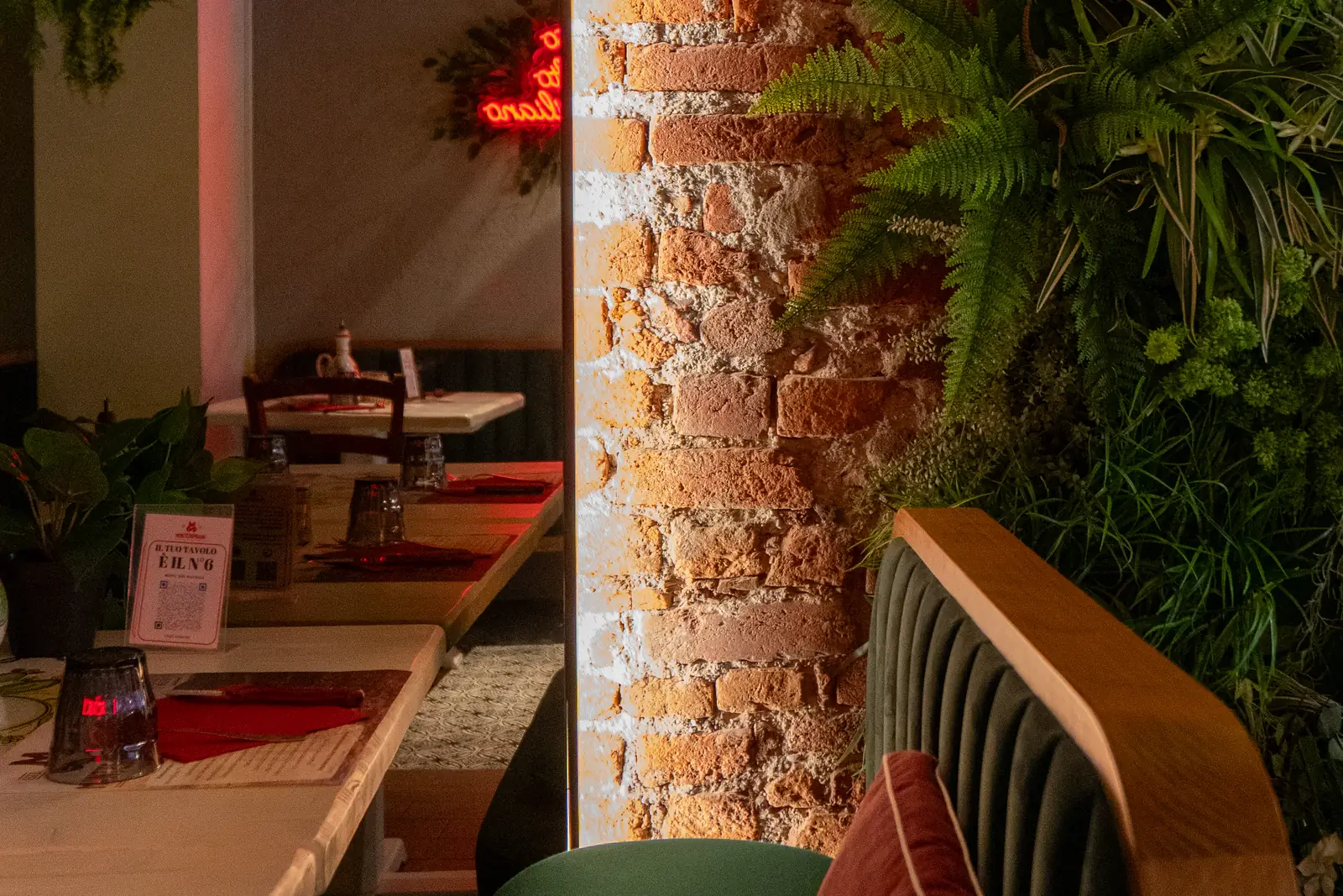 Macelleria con cucina MonteSoprano: la sala di Milano con il pilastro di mattoni, la parete di piante e il divanetto di velluto verde