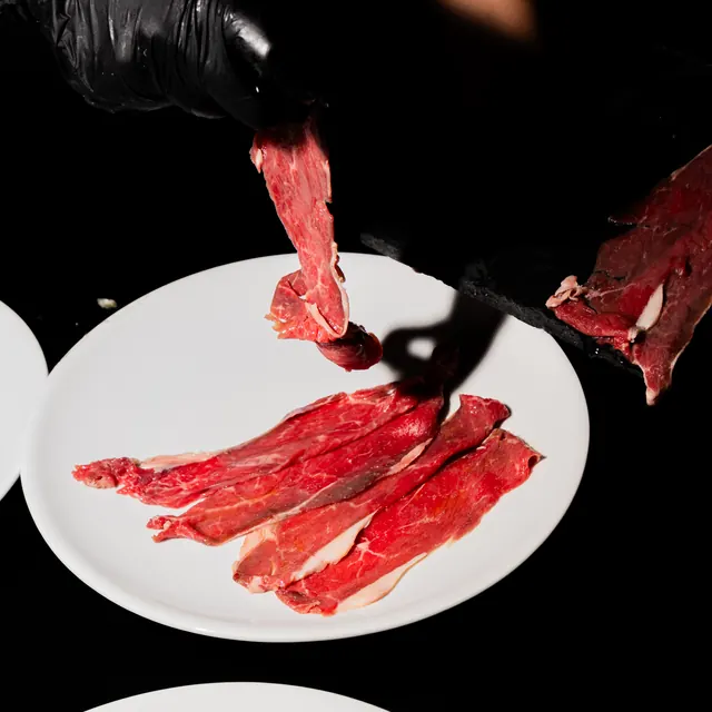 Una mano guantata posa fette di carne cruda su un piatto bianco
